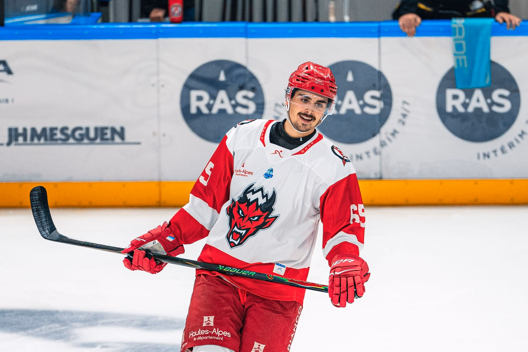 Le n° 65 des Diables Rouges, crosse en main et sourire aux lèvres, sur la glace en maillot blanc et rouge