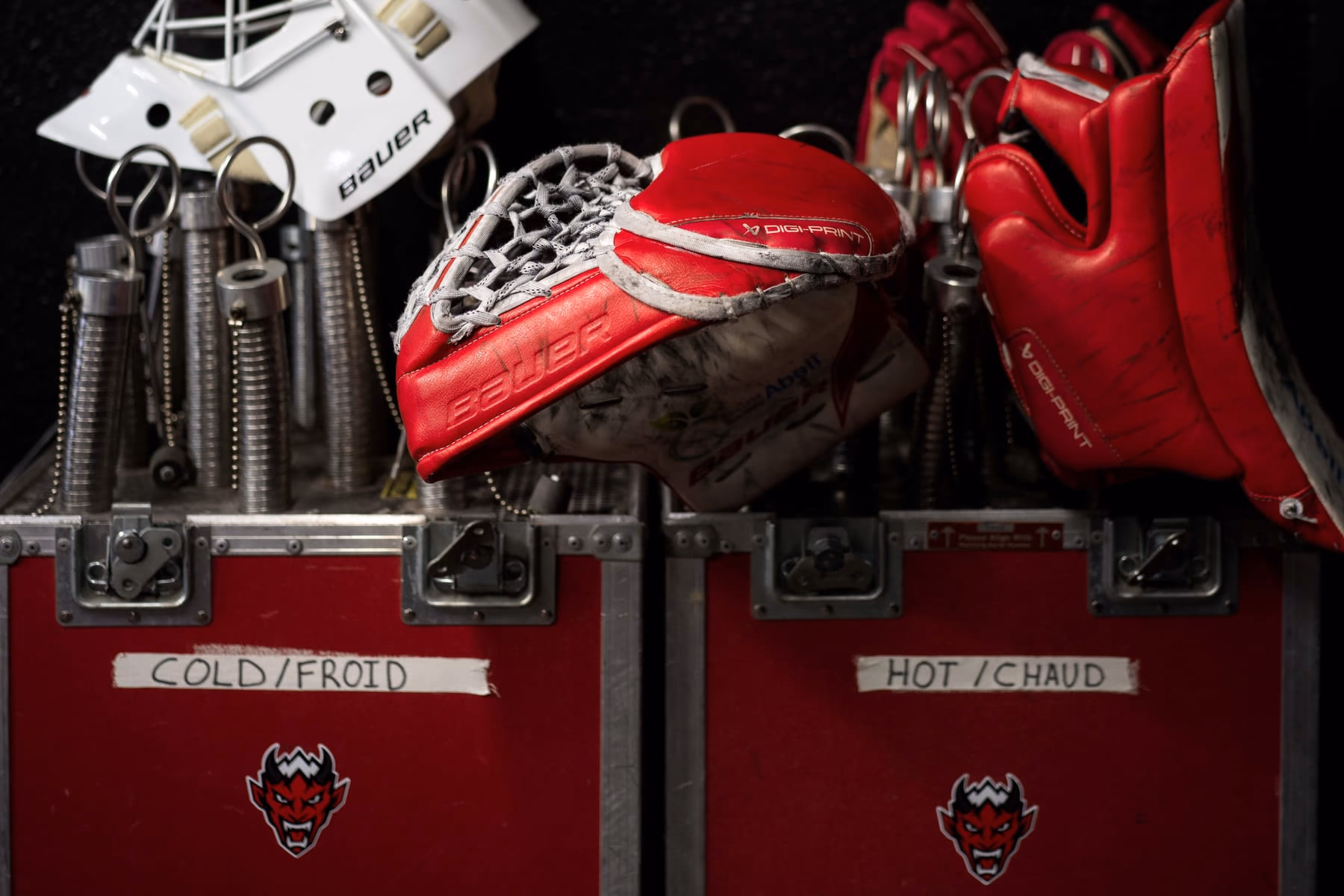 Le matériel du gardien des Diables Rouges, masque blanc, mitaine et bouclier rouges, posé sur deux malles de transport rouges marquées « Cold / Froid » et « Hot / Chaud », frappées du logo du club